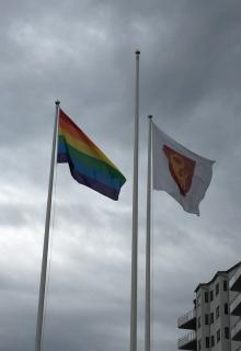 Mot en blyertsgrå himmel vajar Prideflaggan och kommunflaggan.
